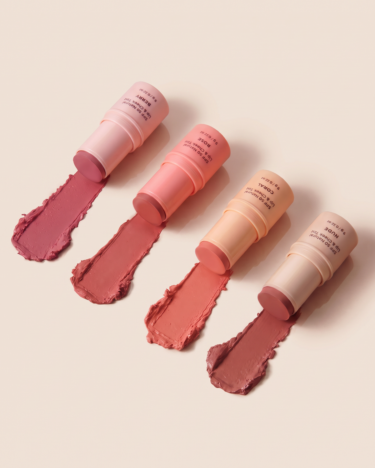 Quatre baumes teintés pour les lèvres et les joues avec protection solaire FPS 50, présentés dans différentes teintes de rose, corail, nude et berry. Les produits sont disposés sur un fond rose pâle avec des échantillons de texture crémeuse correspondant à chaque couleur.